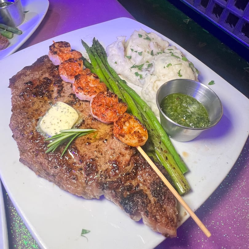 Grilled steak with shrimp skewer, asparagus, mashed potatoes, and green sauce on a white plate.
