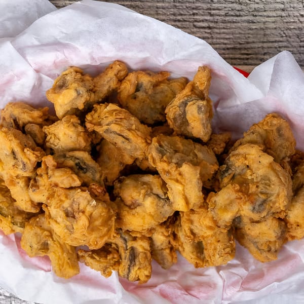 Close-up of golden-brown fried mushrooms in a paper-lined basket from Hungry Like The Wolf.